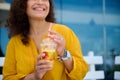 Details on hands of blurred pretty woman holding glass of freshly squeezed orange juice and cutely smiling looking aside