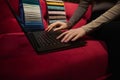 Close-up. Hands of a woman working on laptop, sitting on a red sofa with upholstery fabric samples on background. New home Royalty Free Stock Photo