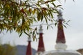 Details of leaves on a tree, with the red cones of three stupas in the background