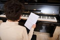 Details on musical notes on white paper sheet in the hands of a teenage boy playing grand piano during music lesson Royalty Free Stock Photo