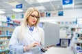 Details of pharmacy drugstore - blonde pharmacist searching for antibiotics on laptop