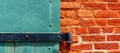 Details of rusty metal hinge holding metal door painted green. Brightly lit old red brick wall. Close up Royalty Free Stock Photo
