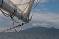 Details of a sailboat, white sail, boom and sheets before blurry background of sea and mountain landscape Royalty Free Stock Photo