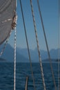 Details of a sailboat, white sail, lifelines and sheets before blurry background of sea and mountain landscape