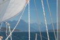 Details of a sailboat, white sail, lifelines and sheets before blurry background of sea and mountain landscape