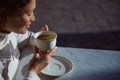 A white porcelain cup with coffee drink in hands of a smiling woman telling fortunes on coffee grounds. People. Leisure