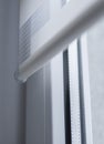 Details of white fabric roller blinds on the white plastic window in the living room. Close up on roll curtains indoor.