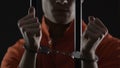 Detained criminal in orange prison jumpsuit showing hands with handcuffs, arrest