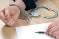 A detainee at the police station. One hand is cuffed, the other is unbuttoned, and there is a pen in his hand for writing