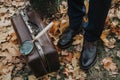 Leather carpetbag is standing on fallen leaves near man legs