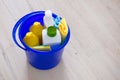 Detergents in plastic bottles, sponges, brush in blue household bucket. Hand in yellow rubber glove. Service concept.