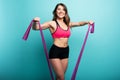 Determinated girl trains with elastic for gym. Happy and joyful expression. Cyan background