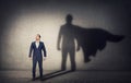 Determined businessman stands confident in a hero stance and casting a brave superhero shadow on the wall behind. Business Royalty Free Stock Photo