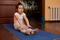 Determined little girl 5-6 years old, exercising barefoot on yoga mat, stretching her body, doing gymnastic exercises