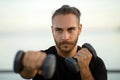 Determined man in fitwear exercises with dumbbells flexing biceps outside Royalty Free Stock Photo