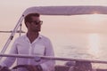 A determined senior businessman in casual clothes and sunglasses enjoys his vacation driving a luxury boat at sunset Royalty Free Stock Photo