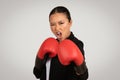 A determined young Asian woman in a black turtleneck and tie poses with red boxing gloves Royalty Free Stock Photo