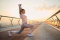 Determined young sportswoman exercising outdoor at dawn. Female athlete in sportswear stretching her arms up, performing squats Royalty Free Stock Photo