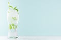 Detox cold water with green mint leaves, ice cubes, striped straw, tonic in elegant glass on white wood table, mint color wall. Royalty Free Stock Photo