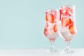 Detox cold water with ripe strawberry slices, ice cubes and tonic in two elegant glasses on white wood table, mint color wall. Royalty Free Stock Photo