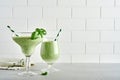 Detox green vegetable juice or smoothie garnished with leaf of fresh basil in coctail glass on light gray slate, stone or concrete
