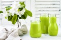 Detox, healthy green smoothie in jars and bottle. White wooden rustic background with apple blossom.