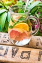 Detox infused citrus water in glass pitcher with oranges, lemons, grapefruits, limes, fresh mint on wood fruit garden box, green p