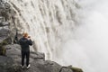 DETTIFOSS, ICELAND - AUGUST 2018: Man in black taking picture of waterfall on cliff edge in Vatnayokull national park