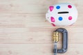 Piggy bank and coins squeezed tightly in a G-Clamp over wooden background Royalty Free Stock Photo