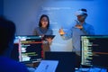 developer uses a VR headset to interact with projected interface designs, while colleagues discuss and code on screens,