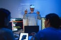 developer uses a VR headset to interact with projected interface designs, while colleagues discuss and code on screens,
