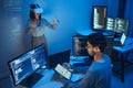 developer uses a VR headset to interact with projected interface designs, while colleagues discuss and code on screens,