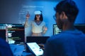 developer uses a VR headset to interact with projected interface designs, while colleagues discuss and code on screens,