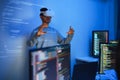 developer uses a VR headset to interact with projected interface designs, while colleagues discuss and code on screens,