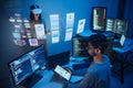 developer uses a VR headset to interact with projected interface designs, while colleagues discuss and code on screens at office