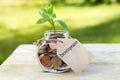 Development. Glass jar with coins, on a wooden table, on a natural background.