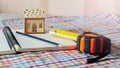 Development of a sketch of the house. Mock up of a wooden house, tape measure and pencil on an open notebook Royalty Free Stock Photo