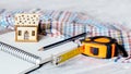 Development of a sketch of the house. Mock up of a wooden house, tape measure and pencil on an open notebook Royalty Free Stock Photo