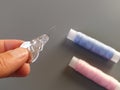 Device for drawing the thread into the eye of the needle. Bobbins with blue and pink threads in the background. A woman holds a Royalty Free Stock Photo