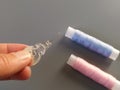 Device for drawing the thread into the eye of the needle. Bobbins with blue and pink threads in the background. A woman holds a Royalty Free Stock Photo