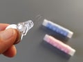 Device for drawing the thread into the eye of the needle. Bobbins with blue and pink threads in the background. A woman holds a Royalty Free Stock Photo