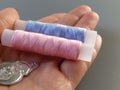 Device for drawing the thread into the eye of the needle. Bobbins with blue and pink threads in the background. A woman holds a Royalty Free Stock Photo