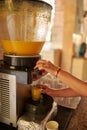 A device for squeezing orange juice in hotels. Female hands filling a glass with freshly squeezed orange juice. Catering in hotels