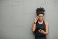 Devices for sport. Happy african american girl with headphones, fitness tracker, looks at smartphone and chooses music