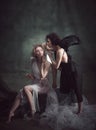 Devilish woman whispering to naive angel. Portrait of two women, angel and demon against dark, green, vintage background Royalty Free Stock Photo