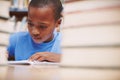 Devoting all his attention to the books. A cute young boy writing a story in the library while surrounded by books. Royalty Free Stock Photo