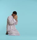 devout Muslim man kneels in pray, hands covering face in act of Namaz, fundamental Islamic ritual. Isolated against blue