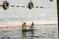 Dhaka, Bangladesh, February 24 2017: Two men ride their wooden boat between large ships on Buriganga River in Dhaka Royalty Free Stock Photo