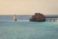 Dhow boat sails in the ocean near beautiful thatch stilt house restaurant at sunset Royalty Free Stock Photo