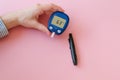 Diabetes concept. Female hand holding glucometer with test strip, lancelet on pink background. Royalty Free Stock Photo